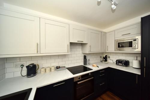 una cocina con armarios blancos y electrodomésticos blancos en Pinfold Suite - Chester Road Apartments By, en Macclesfield