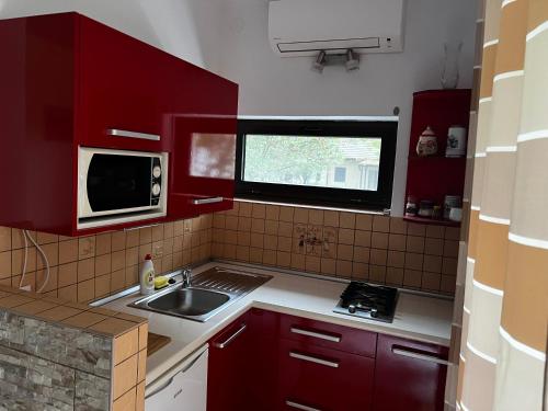 a kitchen with red cabinets and a sink and a microwave at Mediterán Fedett Medencés Apartmanház in Szántód