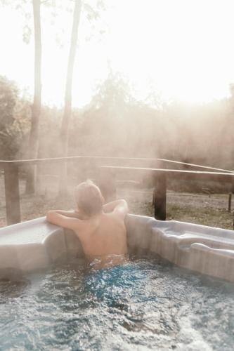 a man in a hot tub in the woods at Riverside Cabins in Shrewsbury