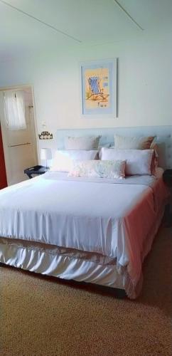 1 dormitorio con 1 cama grande con sábanas y almohadas blancas en Nzima BnB, en Estcourt