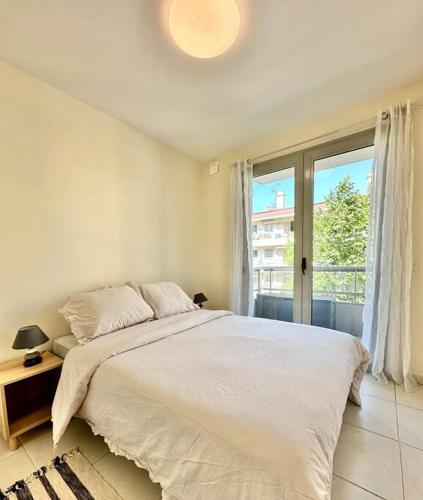 une chambre blanche avec un grand lit et une fenêtre dans l'établissement Cosy holidays - beach, bars & food at 10min walk, à Antibes