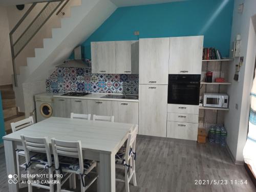 Una cocina con gabinetes blancos y una mesa con sillas. en Casa Mael, en Villasimius