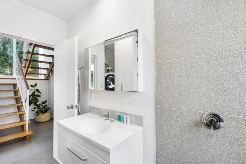 a white bathroom with a sink and a mirror at Coastal Calm is near to the Beach with BBQ in Auckland