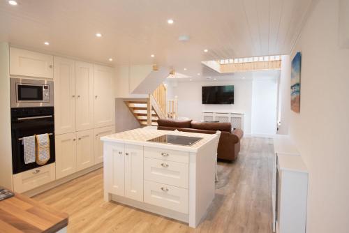a kitchen and living room with white cabinets and a couch at Ardnavaha House - Poolside Cottages in Clonakilty