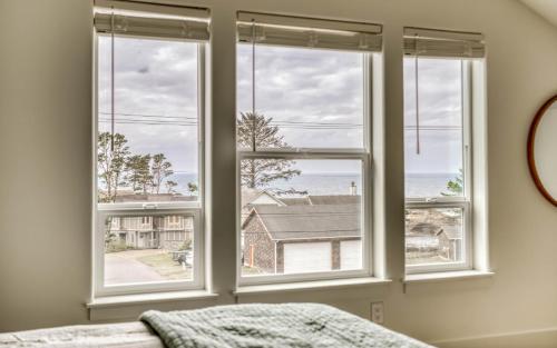 a bedroom with three windows with a view of the ocean at Organic by Nature in Depoe Bay