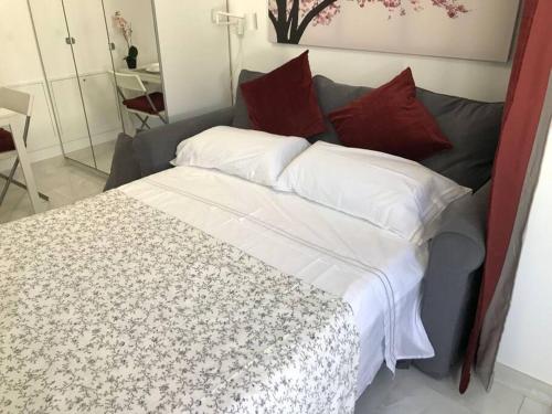 un letto con lenzuola bianche e cuscini rossi in una stanza di Precioso Apartamento nuevo con Jardín privado a Paracuellos de Jarama