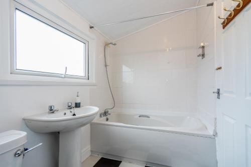 a white bathroom with a tub and a sink at Bright and Modern 4 bed house- TV IN EVERY ROOM in Port Talbot