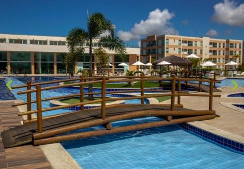 ein Resort-Swimmingpool mit Holzbänken und Sonnenschirmen in der Unterkunft Maraújosflat, Porto de Galinhas in Porto De Galinhas