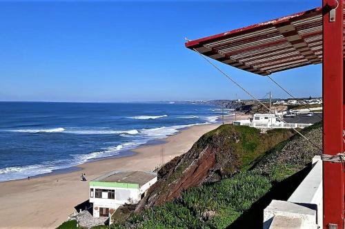 a view of a beach with a red building and the ocean at Pé na Praia in Torres Vedras