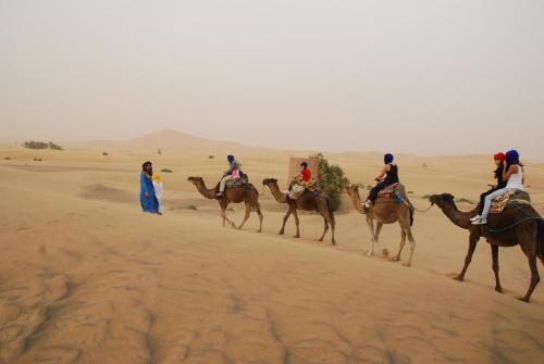 a group of people riding camels in the desert at Riad Dar Poublanc in Merzouga