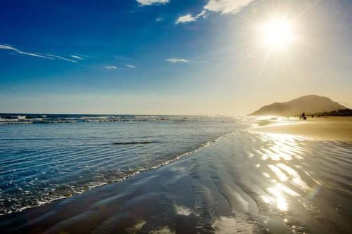 a beach with the sun shining on the water at Apto. com varanda gourmet e piscina aquecida in Bertioga