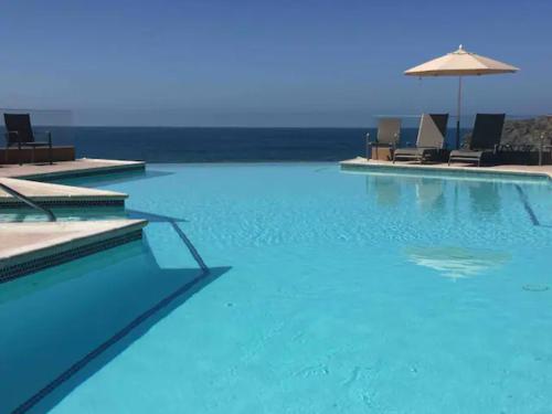 uma grande piscina com cadeiras e um guarda-sol em The Dolphins Ocean Front-Beach 2 BR 2Bth em Rosarito