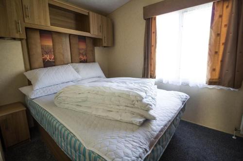 1 dormitorio con 1 cama con sábanas blancas y ventana en 8 Berth Caravan With Wifi At Sunnydale Park In Skegness Ref 35220kc en Louth