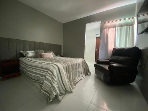 een slaapkamer met een bed en een zwarte stoel bij Duplex agradável com Ar, Internet, Netflix e Estacionamento in Campina Grande