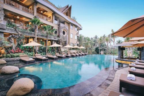 uma piscina num hotel com cadeiras e guarda-sóis em Kuwarasan A Pramana Experience em Ubud