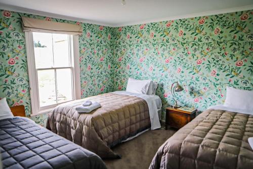 a bedroom with two beds and floral wallpaper at Taieri Bank Cottage - Middlemarch, Otago in Middlemarch
