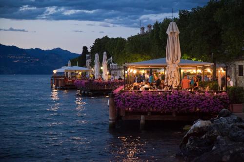 a group of tables with flowers and umbrellas on the water at Hotel Del Porto in Torri del Benaco
