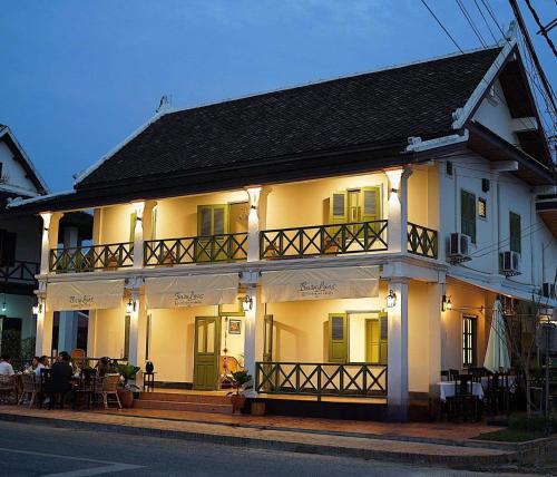 uma casa branca com pessoas sentadas em mesas à frente dela em Barn Laos Luangprabang Hostel em Luang Prabang