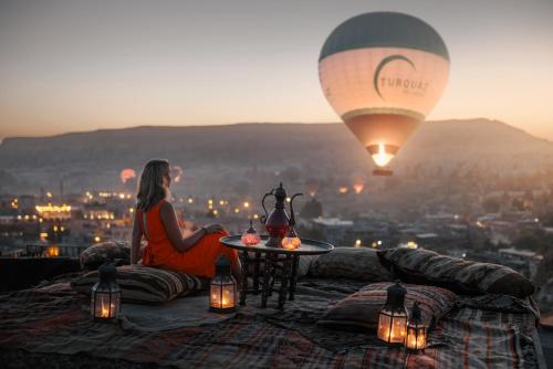 a woman sitting on a ledge with a hot air balloon at Kelebek Special Cave Hotel & Spa in Göreme