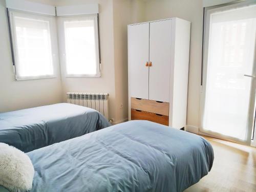 1 dormitorio con 2 camas, armario y 2 ventanas en ESPECIAL HOME apartamento reformado 6 huéspedes en Avilés
