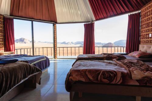two beds in a room with a large window at Wadi Rum Candles Camp in Wadi Rum