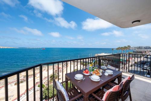 a table on a balcony with a view of the ocean at Islet Promenade Seafront Apartment with large Corner Terrace by Getawaysmalta in St. Paul's Bay
