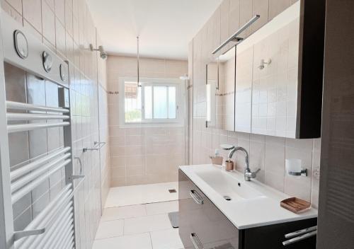 ein weißes Bad mit einem Waschbecken und einer Dusche in der Unterkunft Maison Léon in Ychoux