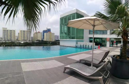 a pool with two chairs and an umbrella and a building at Setapak @ Zeta Suite in Kuala Lumpur