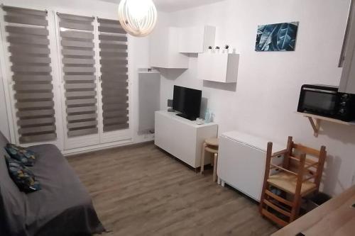 un salon blanc avec une télévision et un bureau avec une chaise dans l'établissement Studio 4 personnes, aux Angles