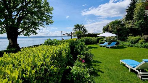 two chairs and an umbrella on a lawn next to the water at Boutique Hotel Villa am See in Hagnau