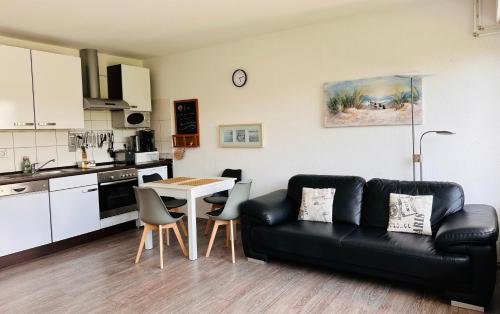 a living room with a black couch and a kitchen at FeWo Seeluft - Hooksiel in Wangerland