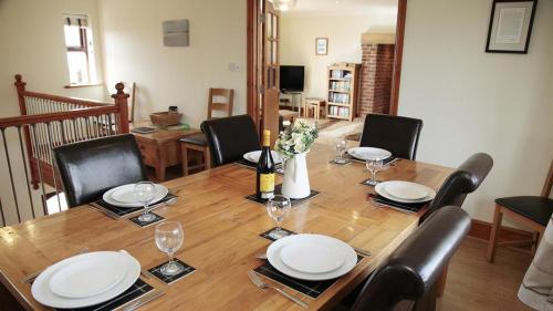 a wooden table with chairs and white plates and wine glasses at Barcud Lodge, Llangennith in Llangennith