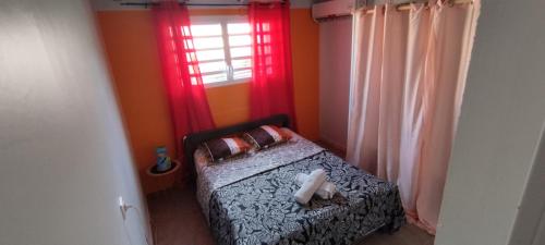 um quarto com uma cama com cortinas vermelhas e uma janela em LASYMPHO - Séjour de repos à la campagne em Le François