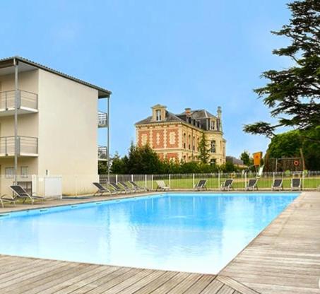 une piscine avec des chaises et un bâtiment en arrière-plan dans l'établissement Le Sea Breeze La Rochelle 44m2 - 2 chambres - 6 prs - Piscine, à Lagord