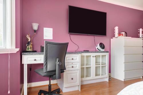 a bedroom with a desk and a tv on a pink wall at Fraser River Richmond Bed and Breakfast in Richmond