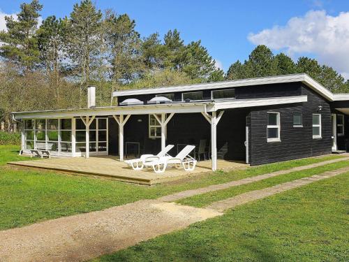 une maison noire avec une terrasse et des chaises. dans l'établissement 8 person holiday home in Hals, à Øster Melholt
