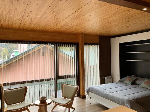 ein Schlafzimmer mit einem Bett und Stühlen sowie einem großen Fenster in der Unterkunft HUEPIL ll, Monoambiente centrico in San Martín de los Andes