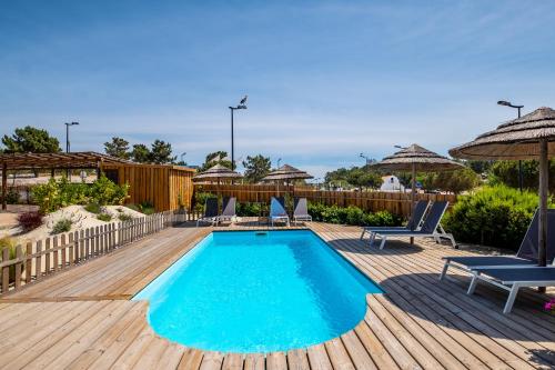 a swimming pool on a wooden deck with chairs and umbrellas at Flow Rooms in Comporta
