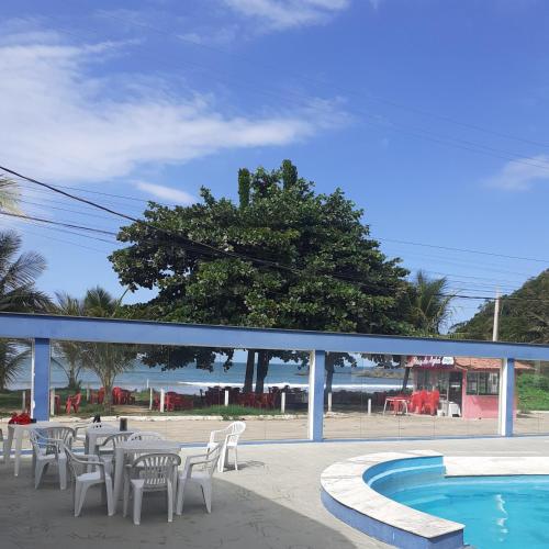 a pool with white chairs and a table and a tree at Cobertura de Frente Para o Mar e Piscina Village das Ondas in Piúma