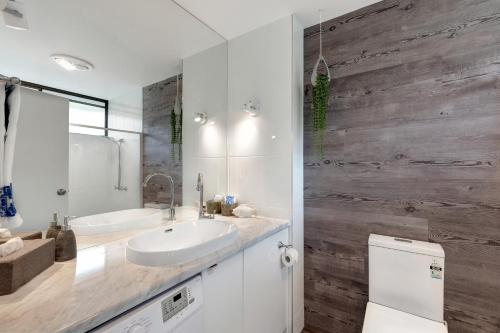a bathroom with a white sink and a wooden wall at OCEAN VIEWS 16 pool & Spa Wi-FI in Airlie Beach