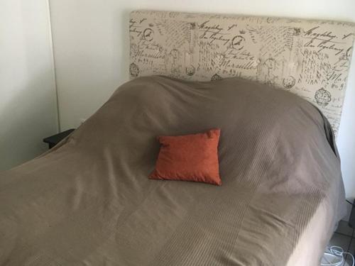 - un oreiller orange assis sur un lit avec une couverture dans l'établissement Hyères : T2 avec clim, piscine & parking au Port - FR-1-335-190, à Hyères