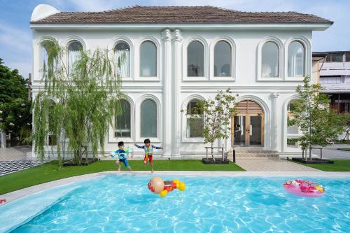 two children playing in a swimming pool in front of a house at Arpo Pool Villa Riverside Bangkok in Bangkok