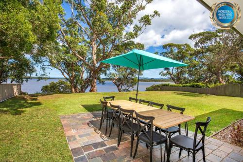 a wooden table with chairs and a blue umbrella at Curleys Outlook I Pet Friendly Waterfront in Culburra Beach