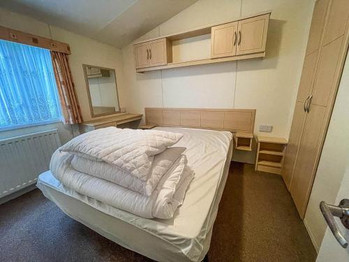 a small bedroom with a bed with white sheets at Caravan At Highfield Grange With Decking, Sleeps 6 Ref 26446ba in Clacton-on-Sea