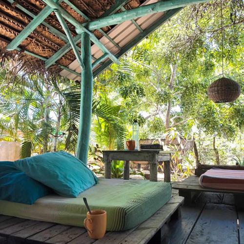 een bed op een houten terras met een tafel en bomen bij The Jungle House in Arugam Bay