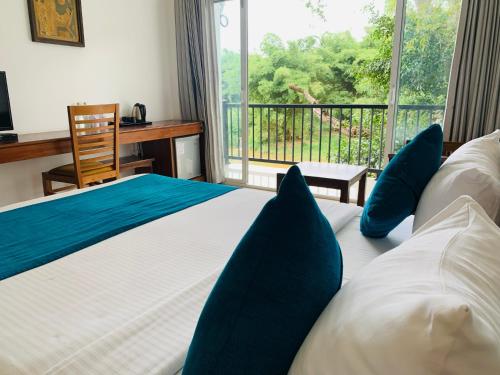a bedroom with a bed with blue pillows and a window at Hotel Gangaaddara in Kandy