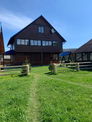 a large wooden house with a green field in front of it at Під Явором in Vorokhta