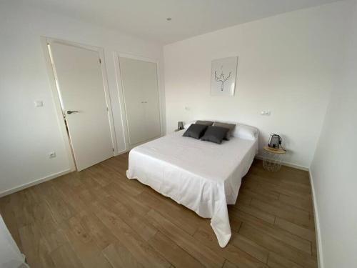 a white bedroom with a white bed and wooden floors at Apartamento Paradis con encanto y vistas al mar in Vinaròs