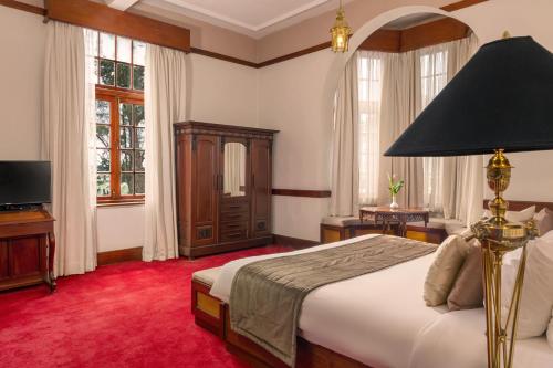 a bedroom with a bed with a lamp and a tv at The Grand Hotel - Heritage Grand in Nuwara Eliya