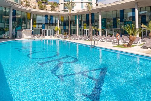 a large blue swimming pool with chairs and a building at Ágora Spa & Resort in Peñíscola